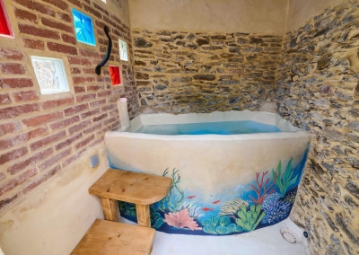 Jacuzzi encastré dans cabanon en pierre avec fresque murale marine.