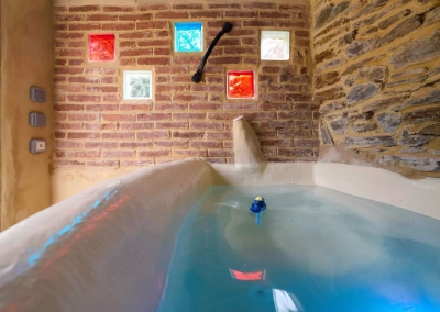 Jacuzzi dans cabanon en pierre avec briques et pavés de verre colorés.