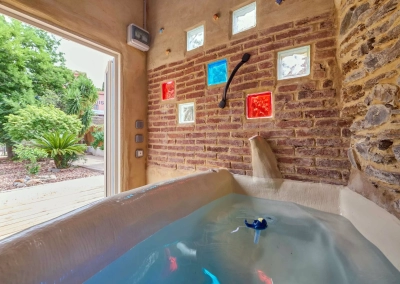 Jacuzzi dans cabanon avec porte ouverte sur le jardin.