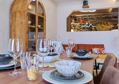 Table dressée dans l’espace repas du logement Le Calypso à Collioure avec salon en arrière-plan.